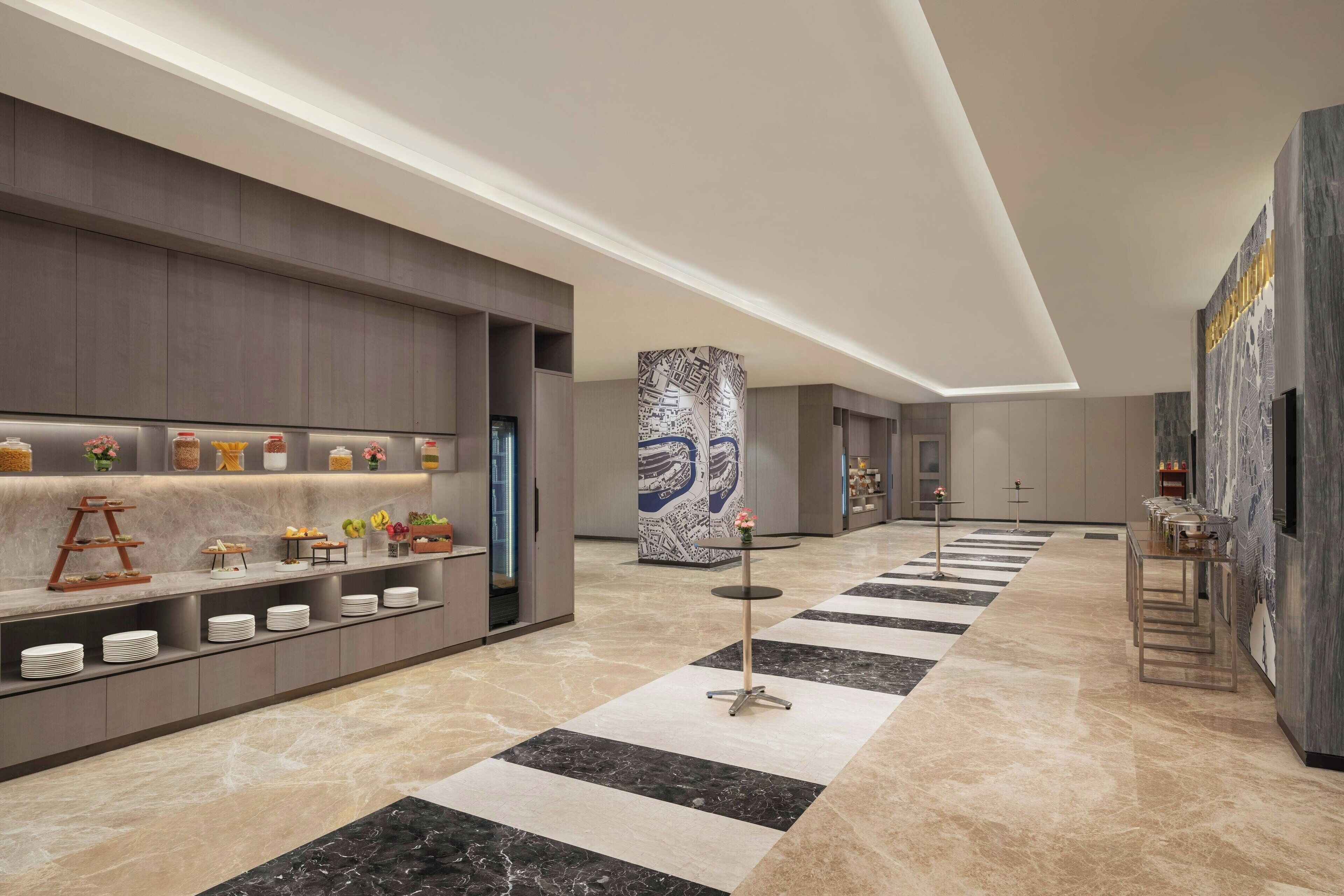 A modern hotel lobby with a long reception desk, a central pillar with a map, and a checkered floor pattern.