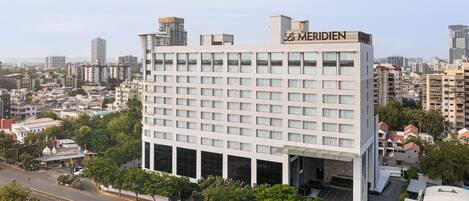 Un hotel de varios pisos con un cartel llamativo de 'Le Meridien', rodeado de otros edificios y follaje.