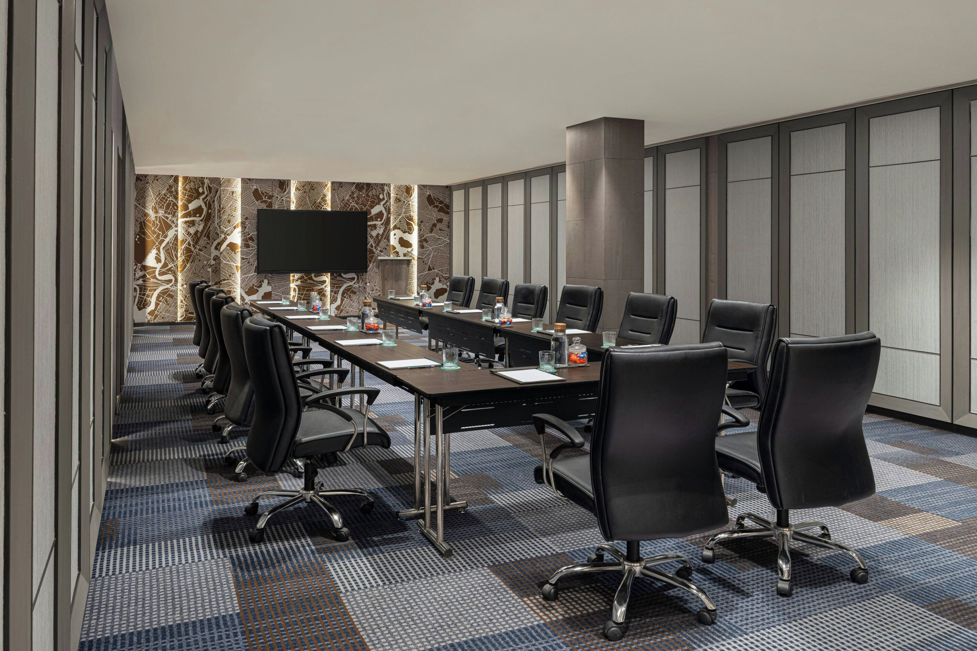 A conference room with a long table, multiple chairs, a flat-screen TV, and a patterned wall.