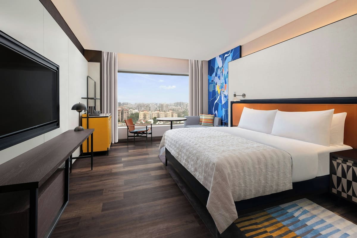 Une chambre d’hôtel avec un grand lit, un bureau avec une télévision, une chaise et une vue sur la ville.