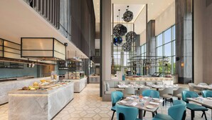 Een modern restaurant met een marmeren bar, blauwe stoelen en een hoge plafond met hangende lampen.