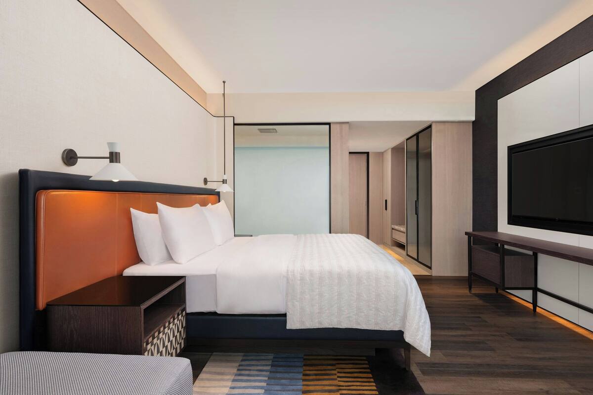 Une chambre d’hôtel moderne, dotée d’un grand lit, d’une télévision et d’un bureau.