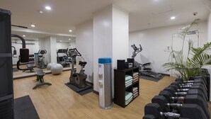 Un gimnasio con equipamiento de ejercicio, un dispensador de agua y mancuernas ordenadas.