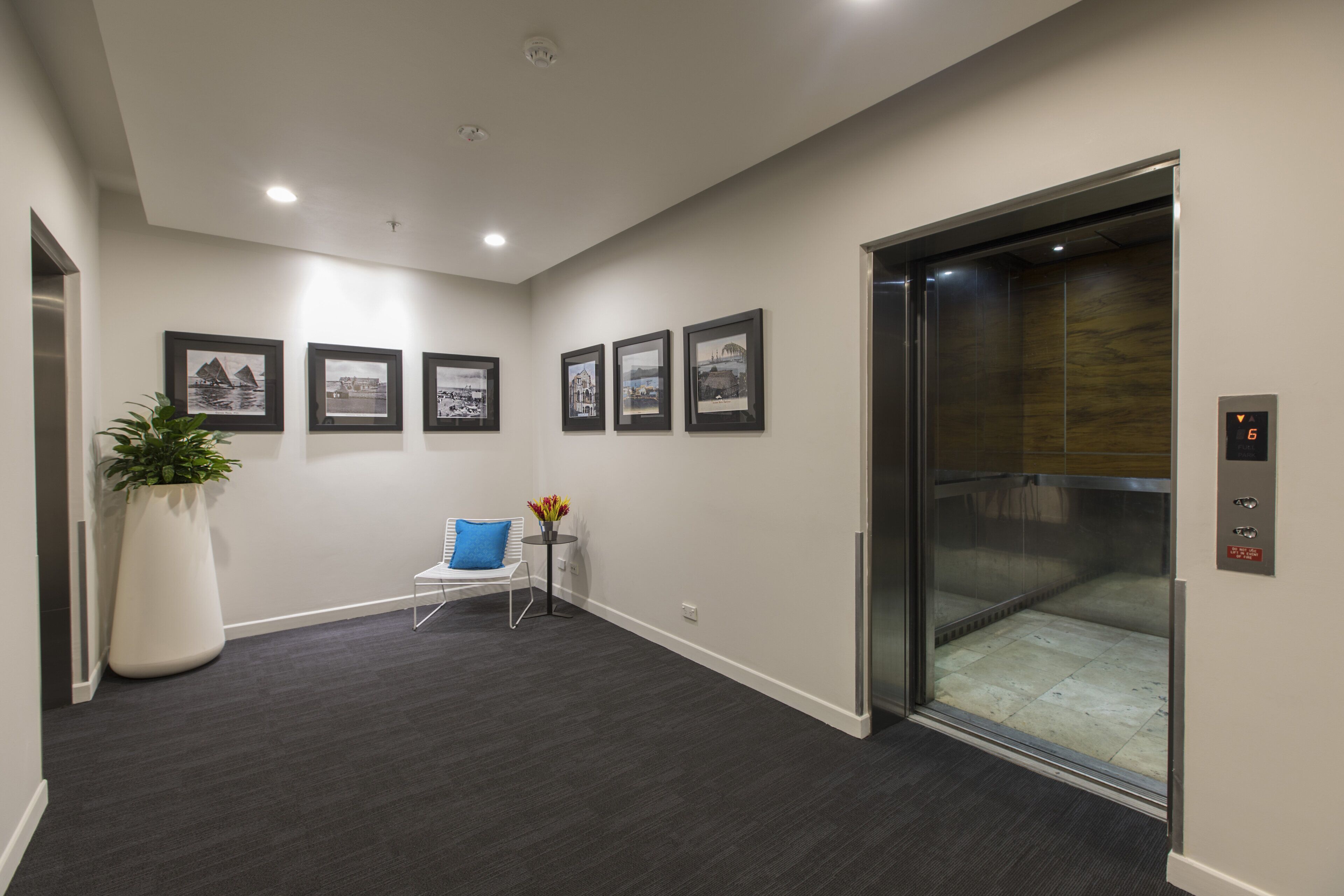 A modern elevator with a digital display, a potted plant, a blue chair, and framed pictures on the wall.
