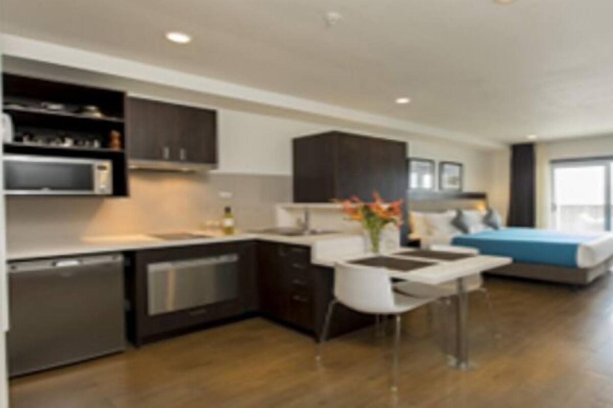 Una cocina moderna con electrodomésticos integrados, un comedor con mesa y sillas blancas, y una cama grande con cabecera azul.
