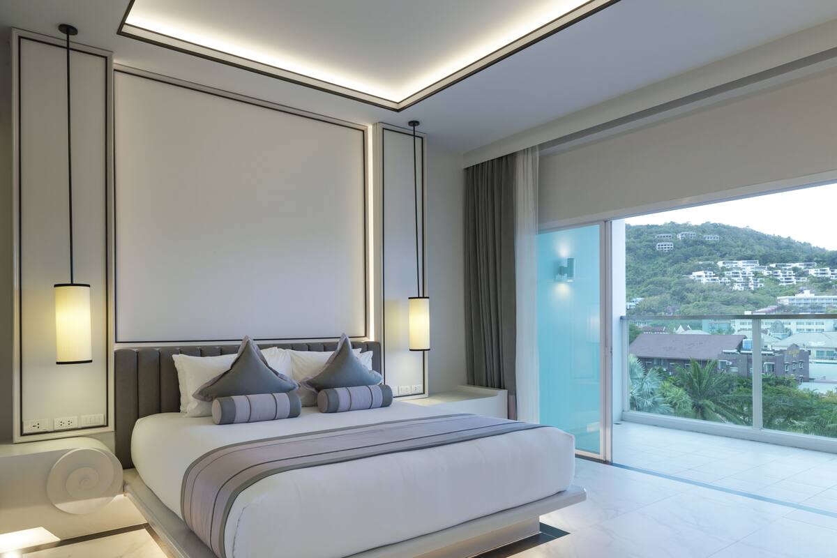 A modern bedroom with a large bed, bedside lamps, and a view of a hillside.
