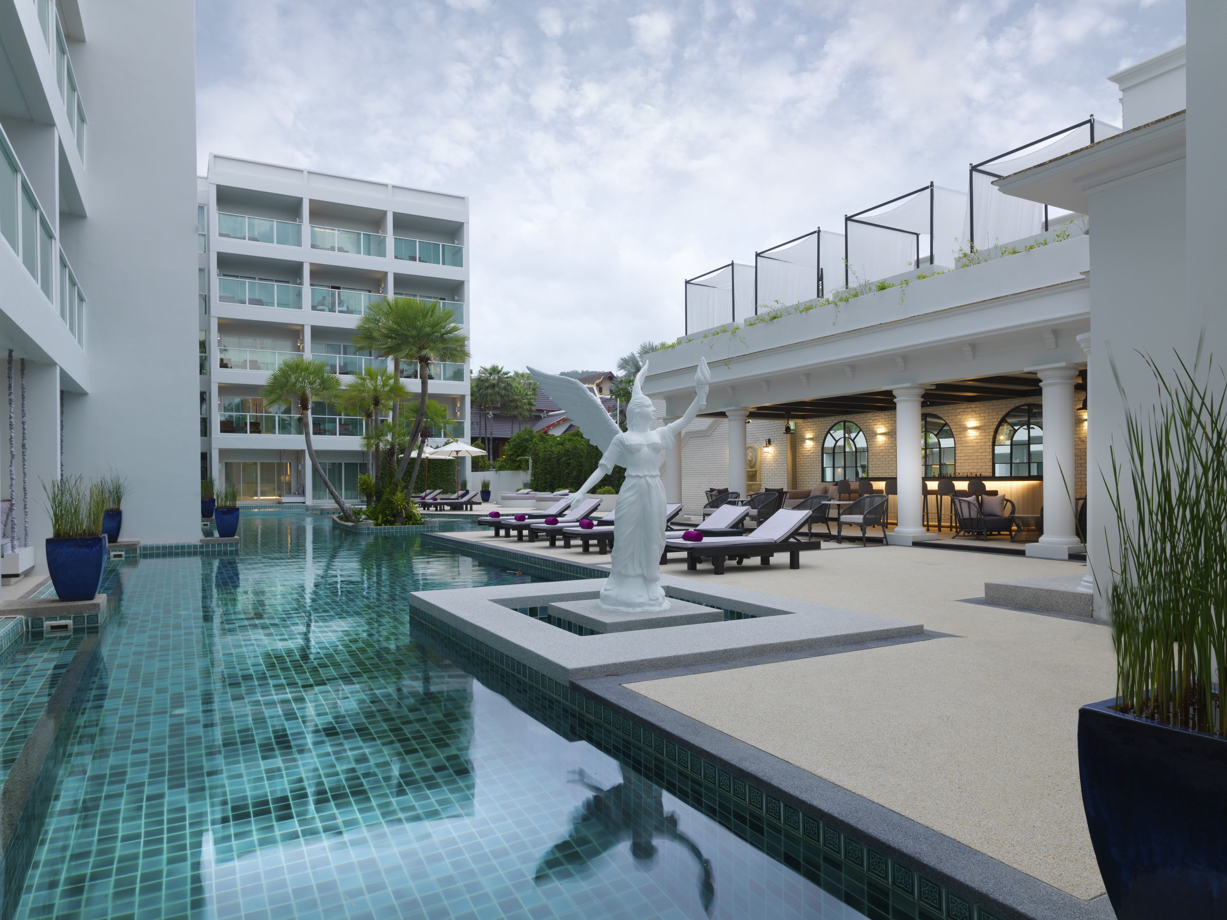 A swimming pool with a statue, lounge chairs, and a building with multiple floors and balconies.