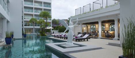 A swimming pool with a statue, lounge chairs, and a building with multiple floors and balconies.