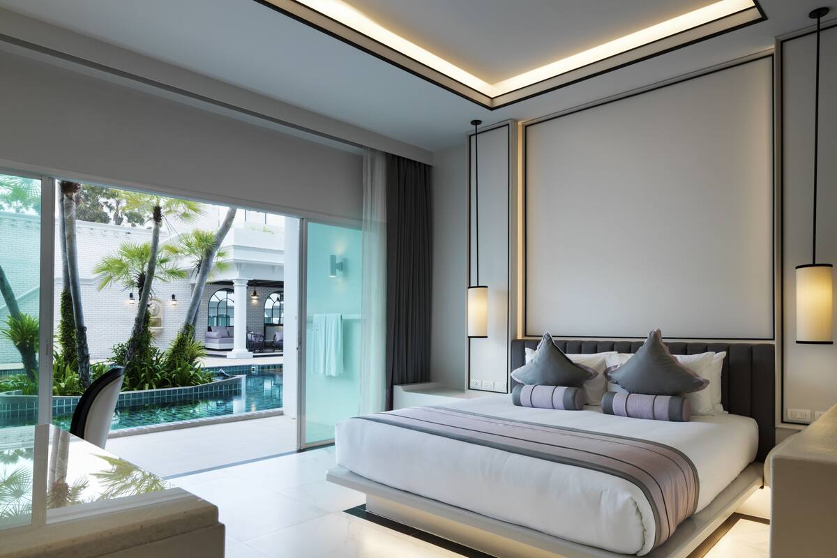 A modern bedroom with a large bed, a view of a pool, and a balcony with plants.