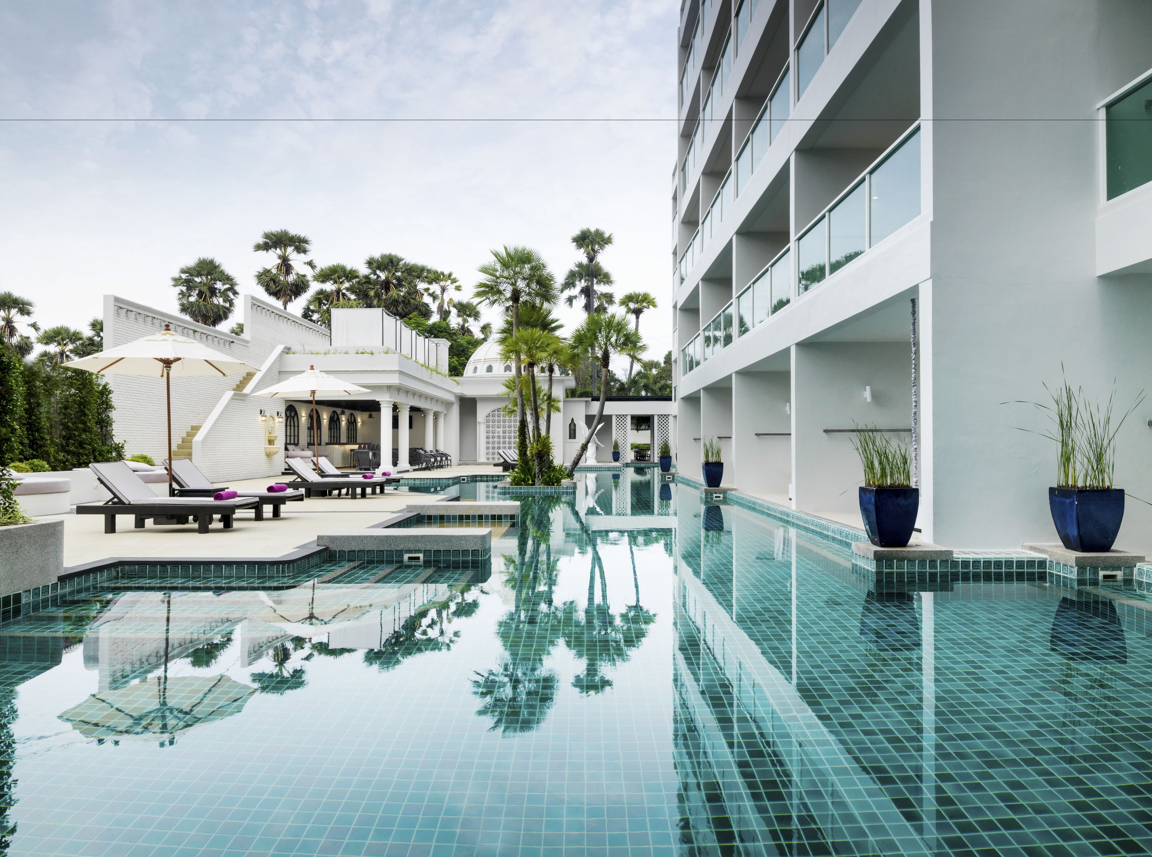 Un hotel moderno con piscina, sillas de descanso y plantas en macetas.