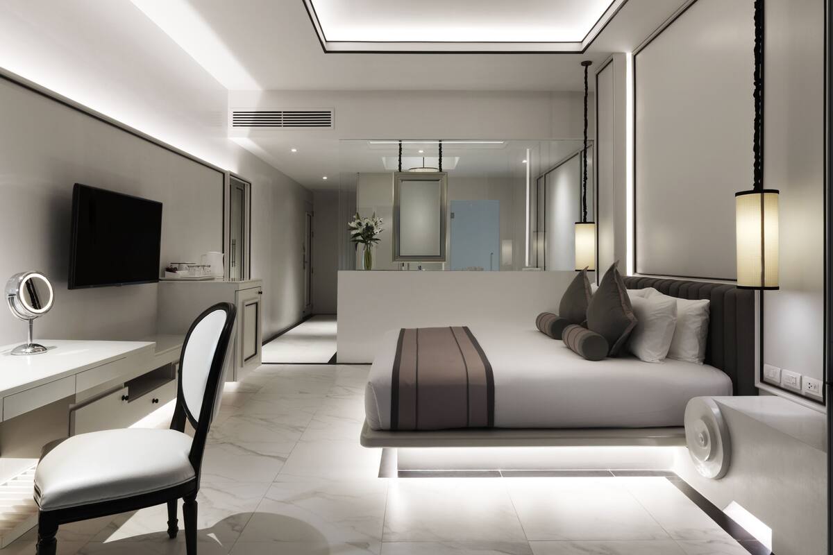 A modern bedroom with a large bed, a desk, a chair, and a TV.