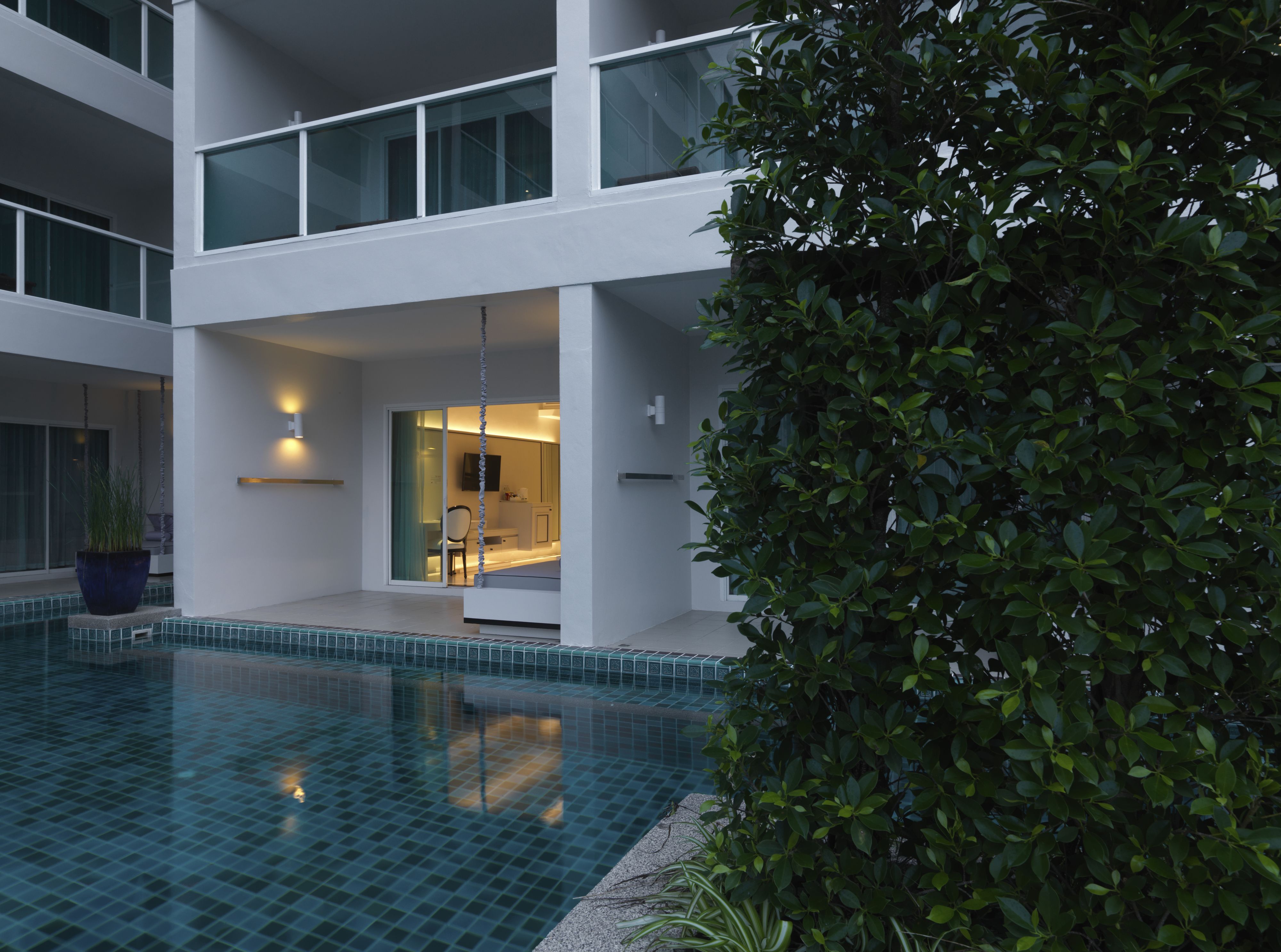 A modern building with a swimming pool, a glass door entrance, and a well-maintained garden.