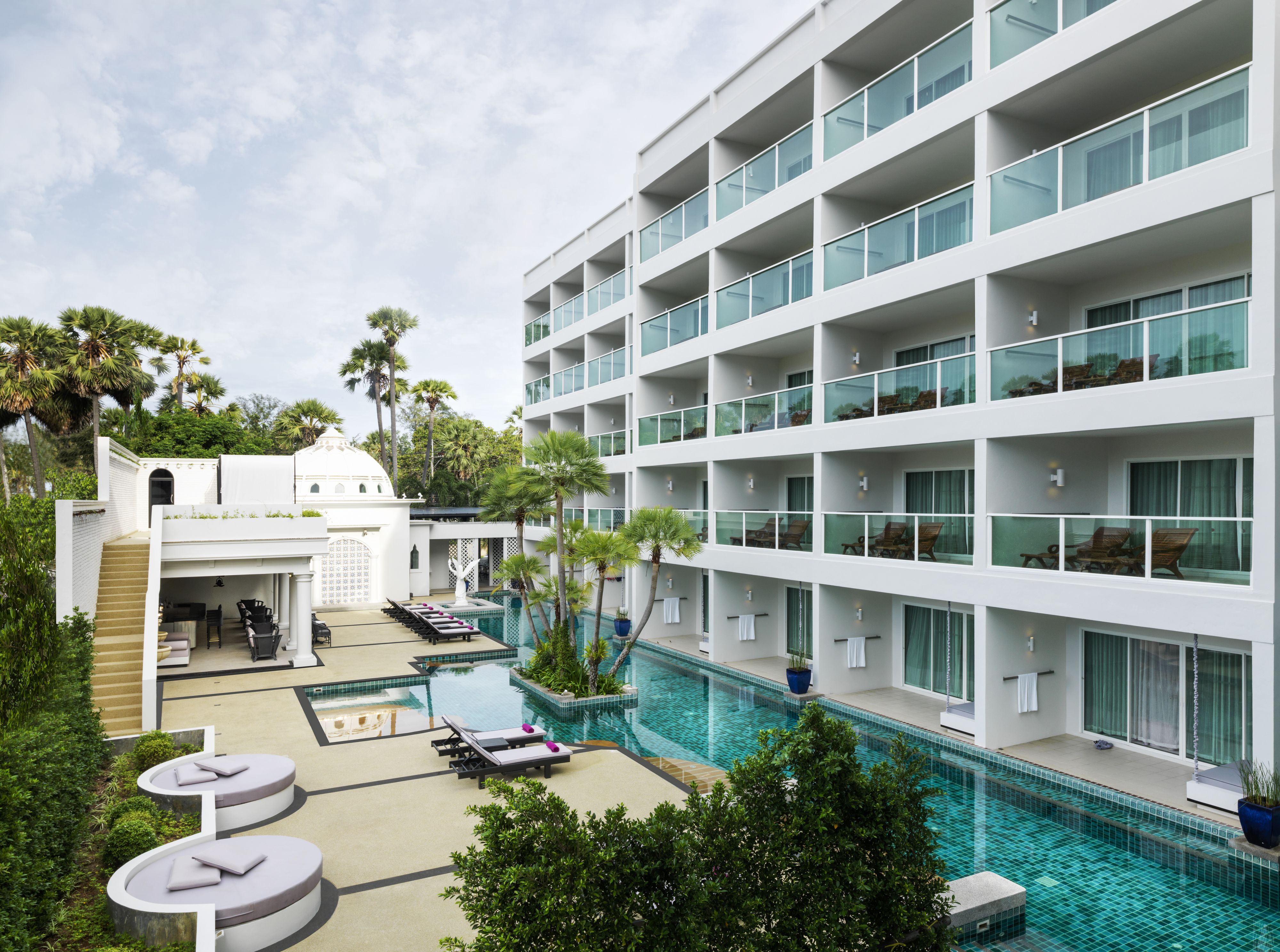 A modern hotel with a rooftop pool, multiple balconies, and lush greenery.