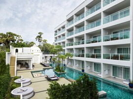 A modern hotel with a rooftop pool, multiple balconies, and lush greenery.