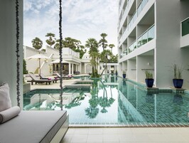 Un hôtel moderne doté d’une piscine, de chaises longues et d’un espace salon abrité.