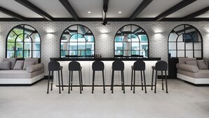 Zona de bar moderna con pared de ladrillo blanco, ventanas arqueadas y mostrador con taburetes.