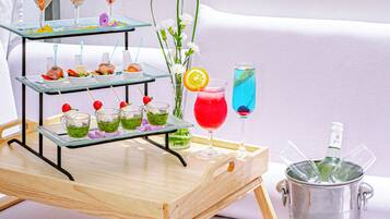 A glass display stand with various drinks and appetizers on a wooden table, a vase with flowers, and a bottle of champagne in a metal bucket.
