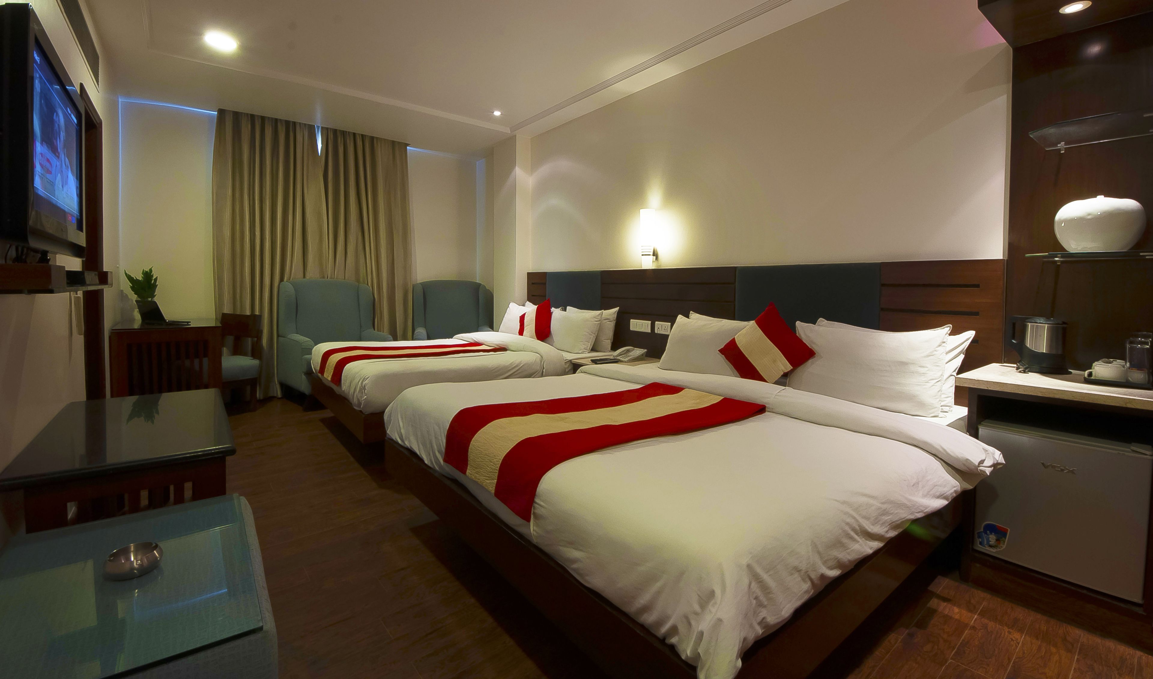 A hotel room with two beds, a desk, a chair, a television, and a coffee maker.