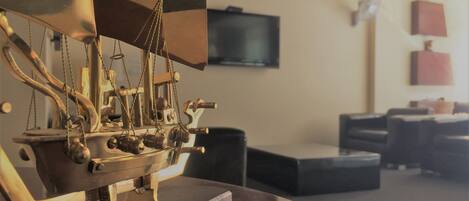 Un modelo de barco de bronce sobre un soporte de madera en una habitación con un televisor en la pared y un sofá al fondo.