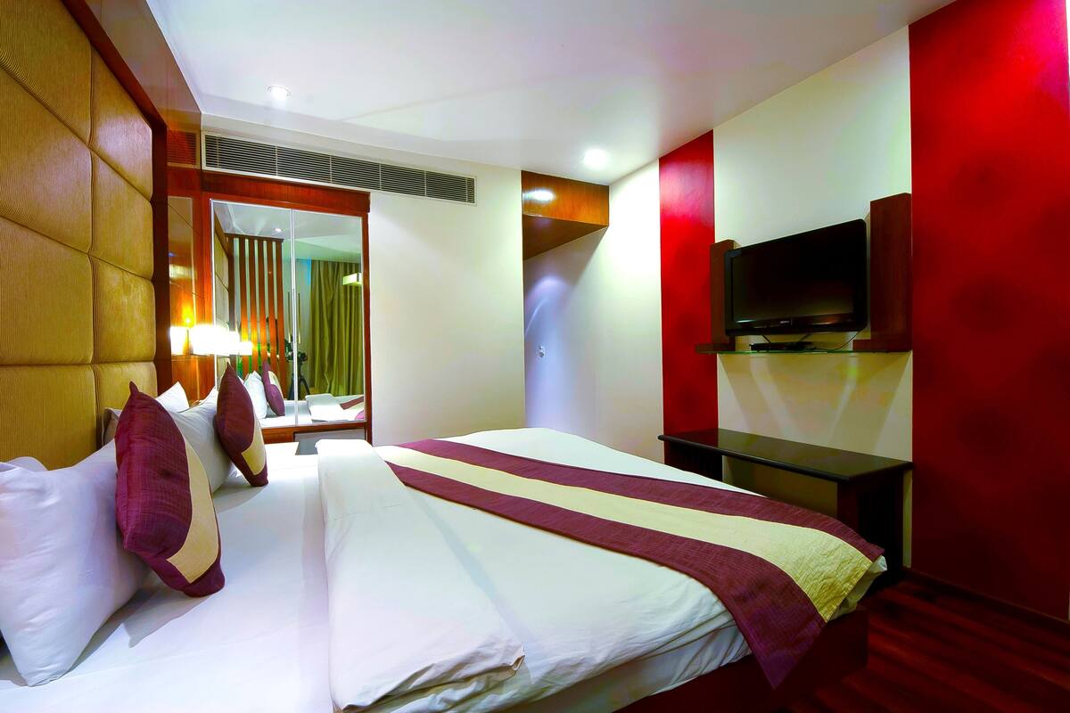 A hotel room with a large bed, a flat-screen TV mounted on the wall, and a mirror above the bed.