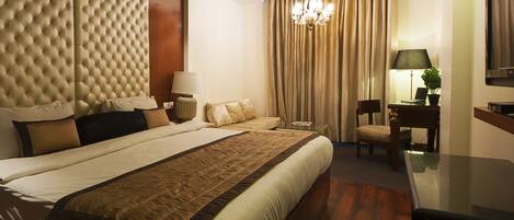 A hotel room with a large bed, a desk, a chair, a lamp, and a chandelier.