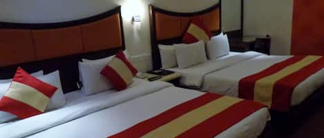 A hotel room with two beds, each with white bedding and red and yellow striped bedspreads. There is a nightstand with a lamp and a phone between the beds.