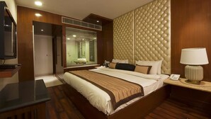 Habitación de hotel con una cama grande, televisión, lámpara de noche y ventana con persianas.
