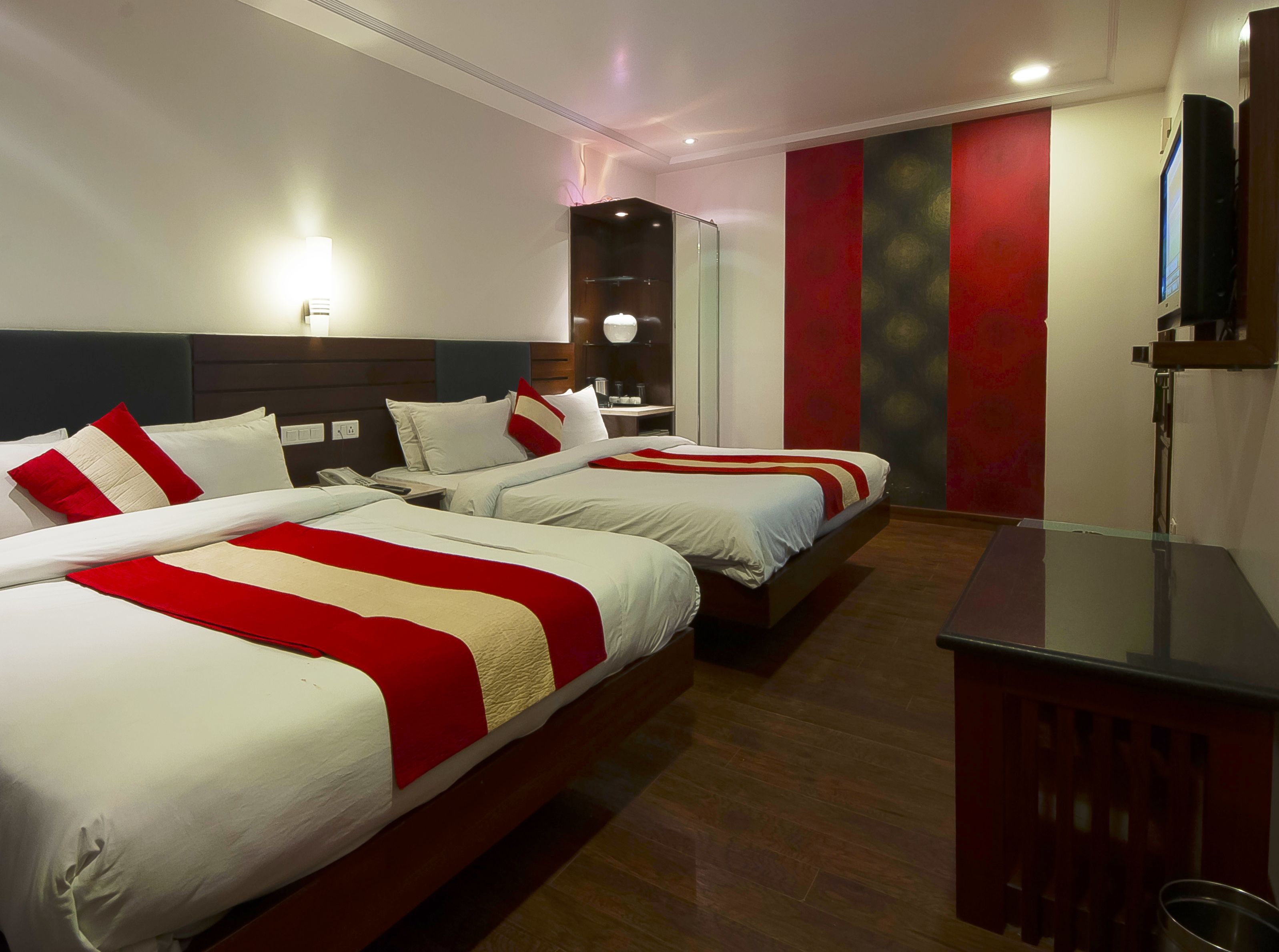 A hotel room with two beds, a desk, a TV, and a red accent wall.