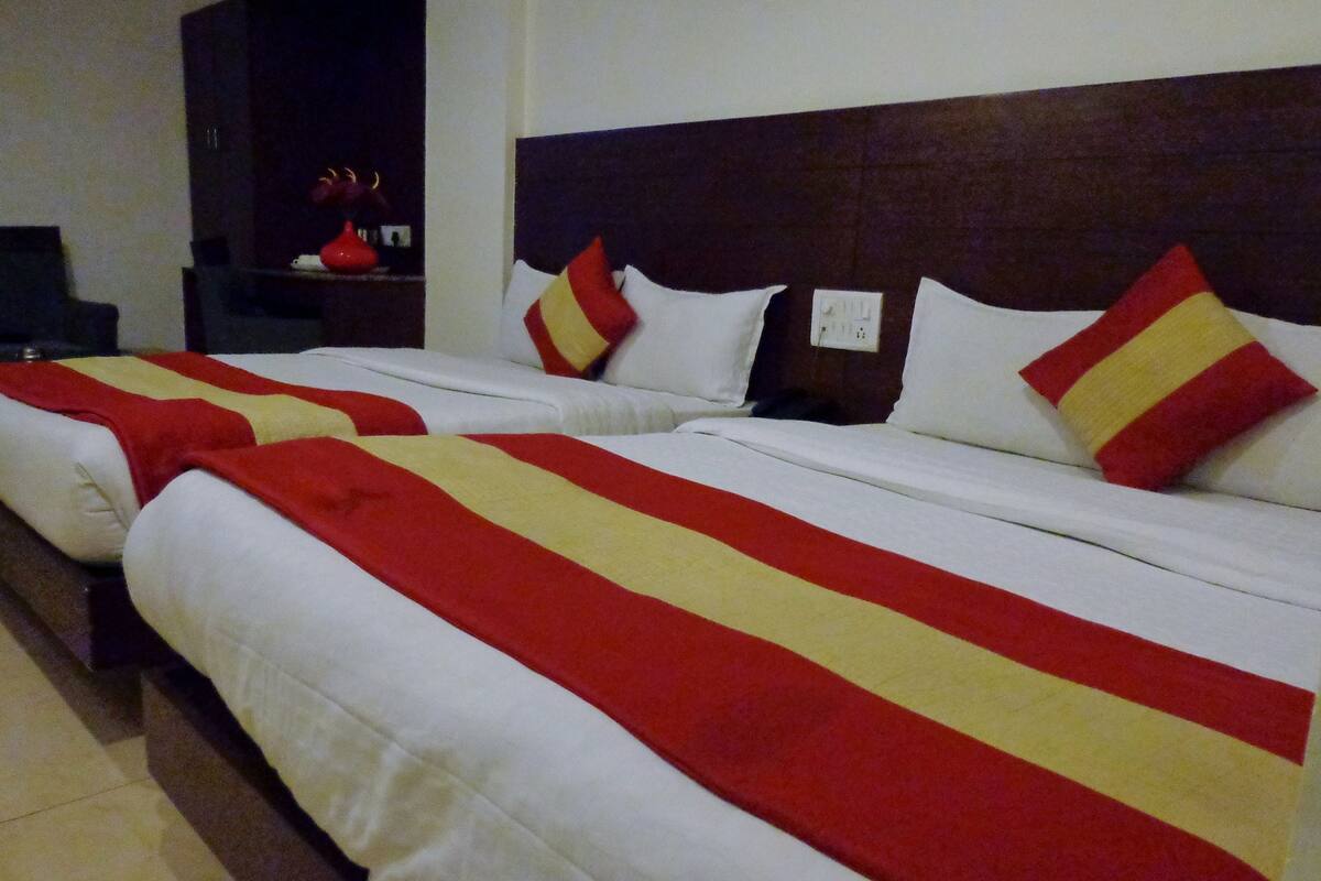 A hotel room with two beds, each with a red and yellow striped bedspread, white pillows, and a dark headboard.