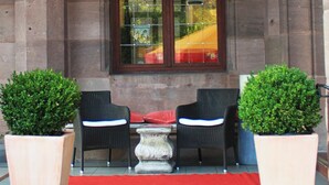 An outdoor seating area with two chairs and a table, a red carpet, and a window with a reflection. - Hotel Deutscher Kaiser (Nuremberg)
