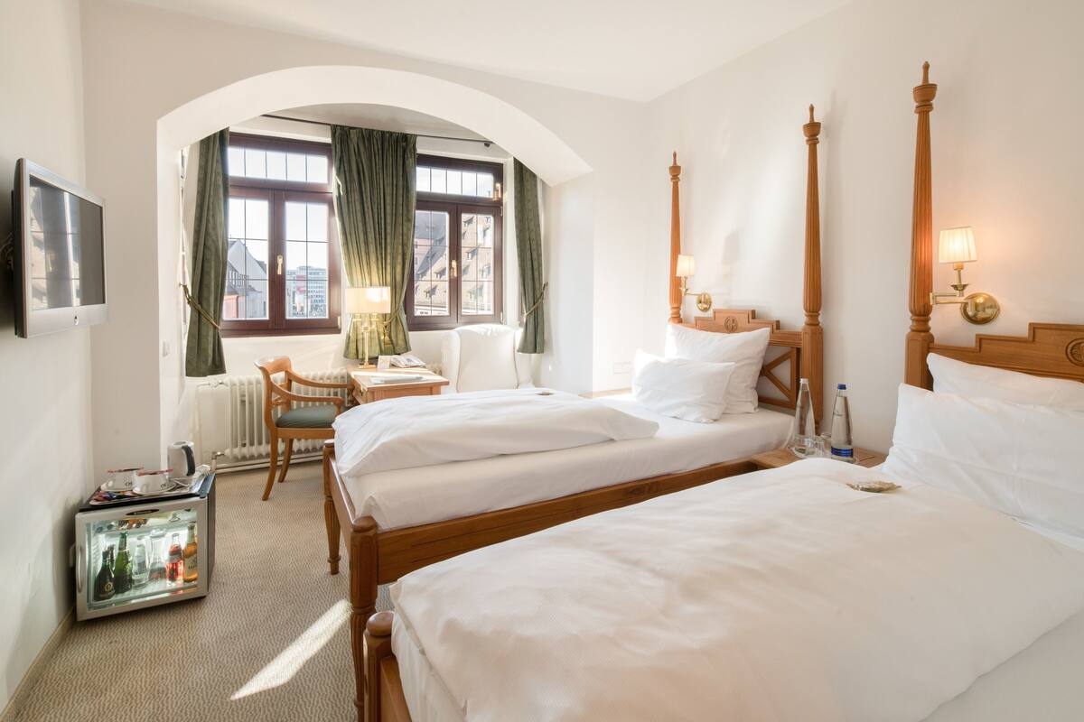 Una habitación de hotel con dos camas, un escritorio, una silla, un televisor y un minibar.