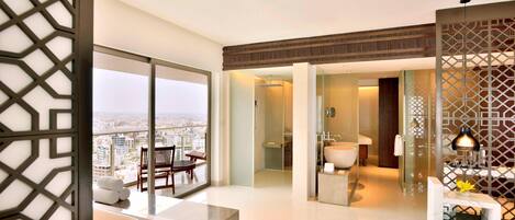 Una habitación de hotel moderna con balcón, baño con bañera y zona de comedor con mesa y sillas.