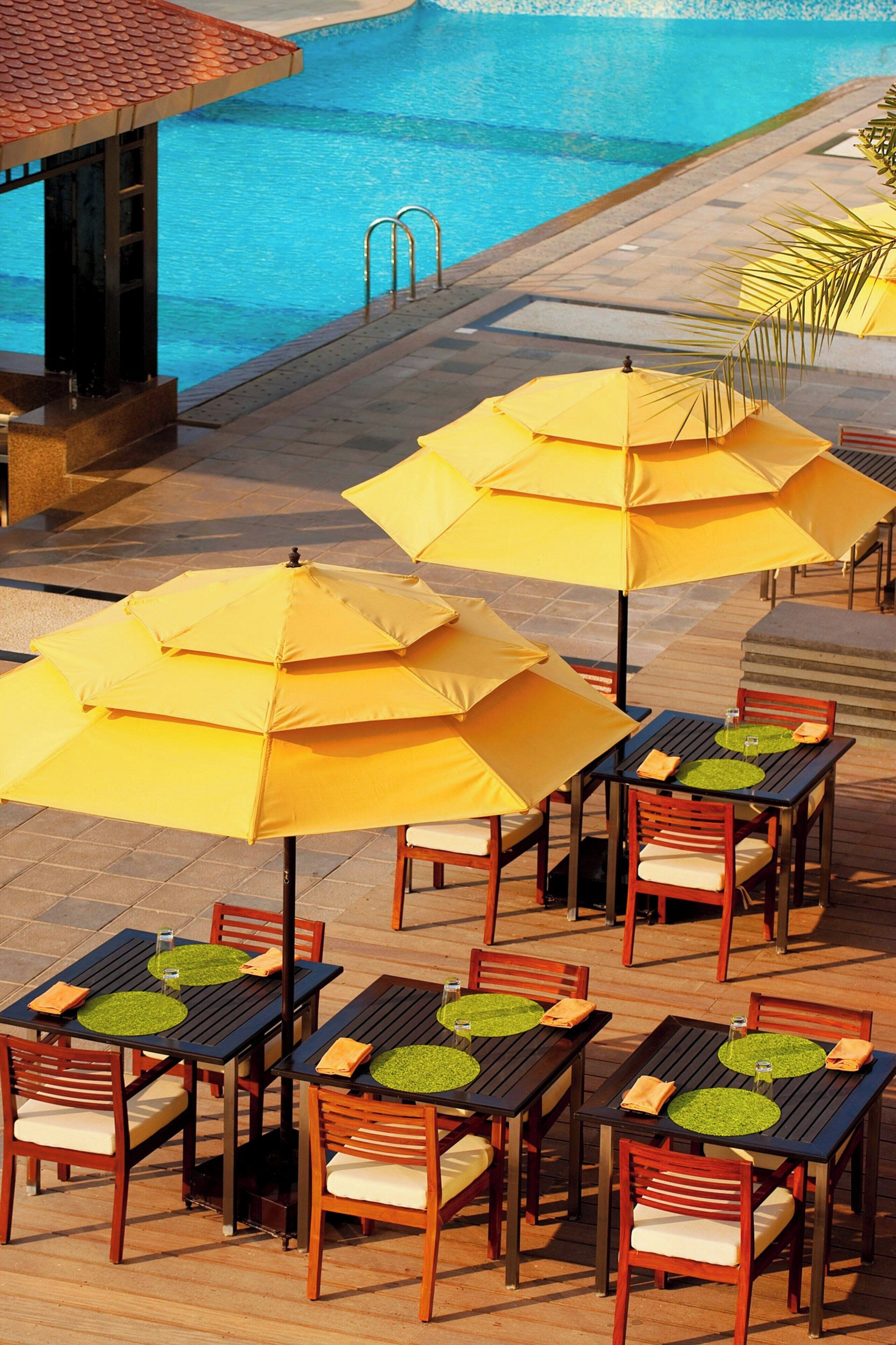 A poolside area with multiple tables and chairs, each with a yellow umbrella.
