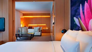 Una habitación de hotel con cama, zona de estar con una mesa y sillas, y televisor montado en la pared.
