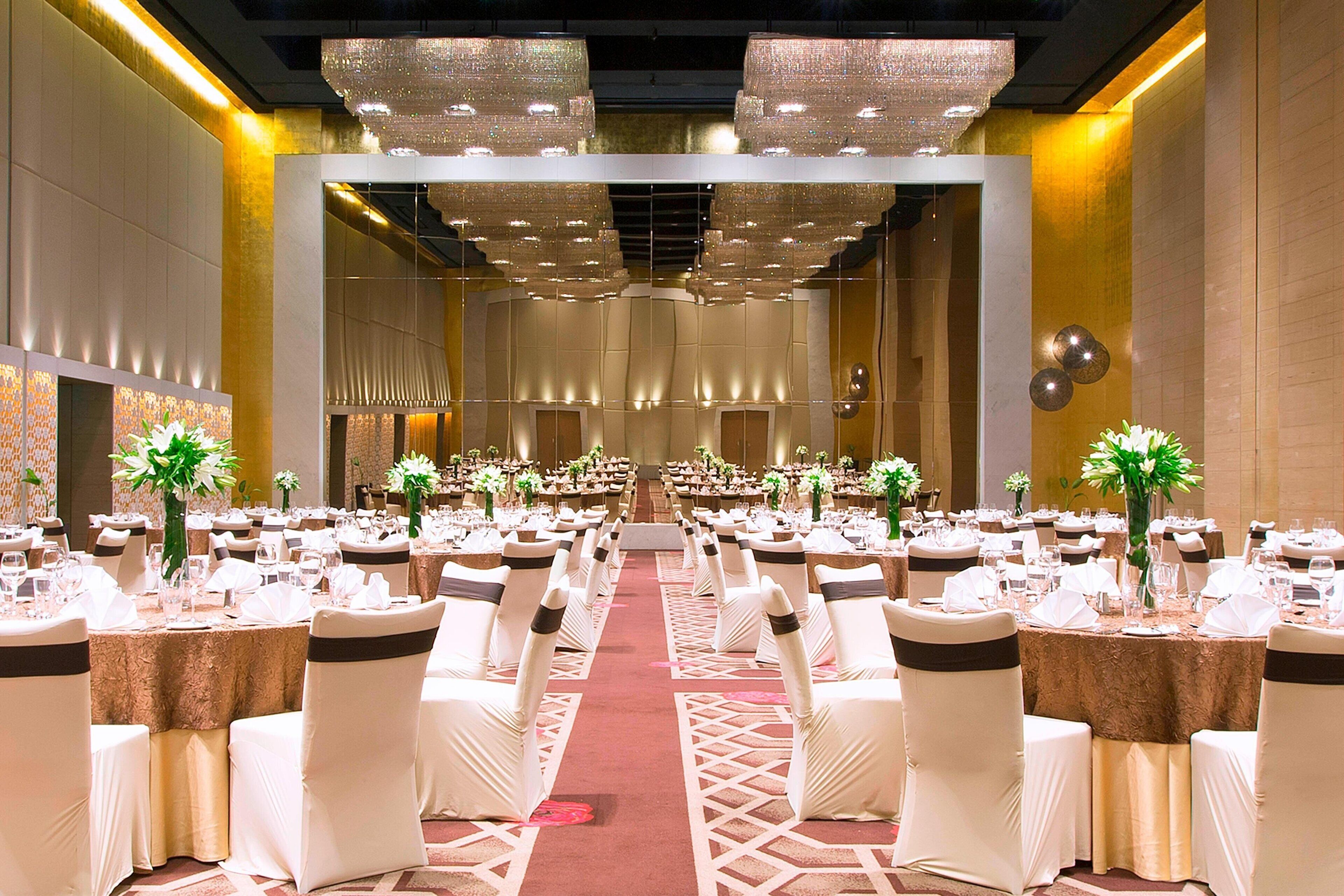 A banquet hall with rows of tables and chairs, a central aisle, and decorative lighting.