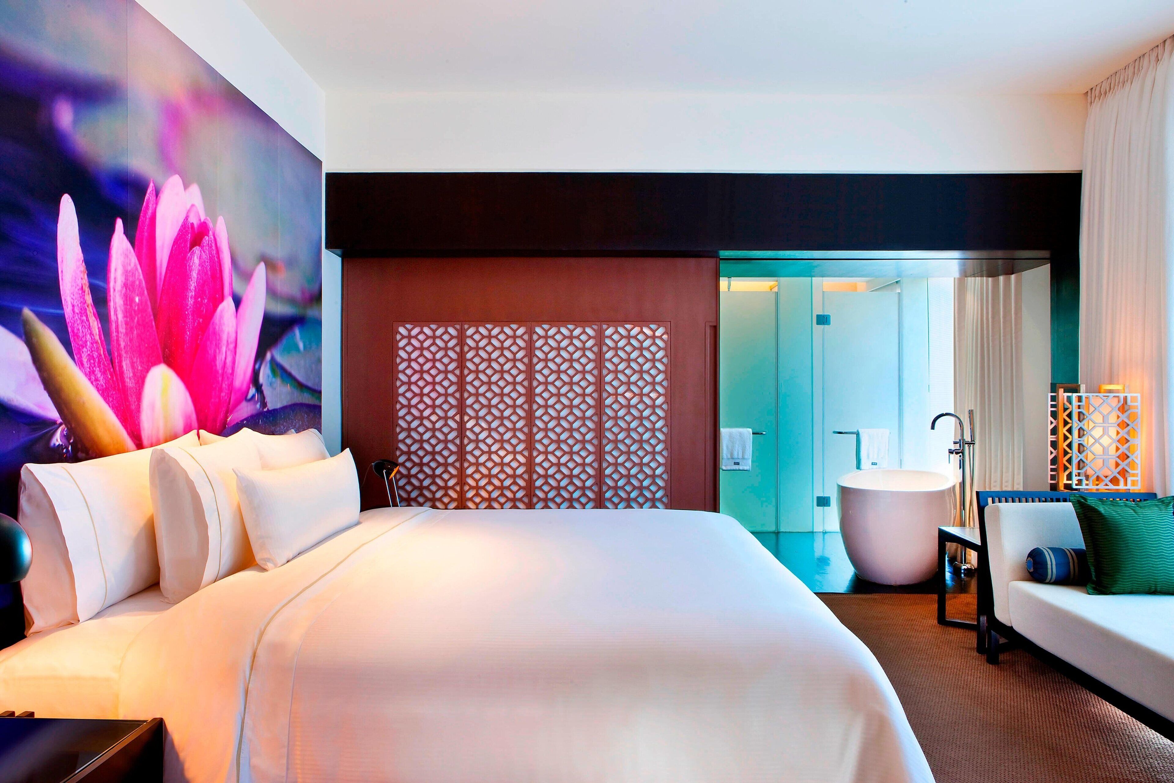 Una habitación de hotel moderna con una cama grande, un sofá, un baño con bañera y una pared decorativa con un mural de flor de loto.