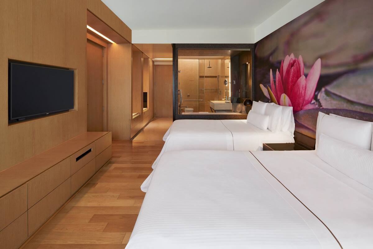 A modern hotel room with two beds, a flat-screen TV, wooden flooring, and a large floral mural.
