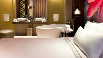 Una habitación de hotel moderna con una cama grande, un espejo redondo, una bañera y un tocador con lavabo y toallero.