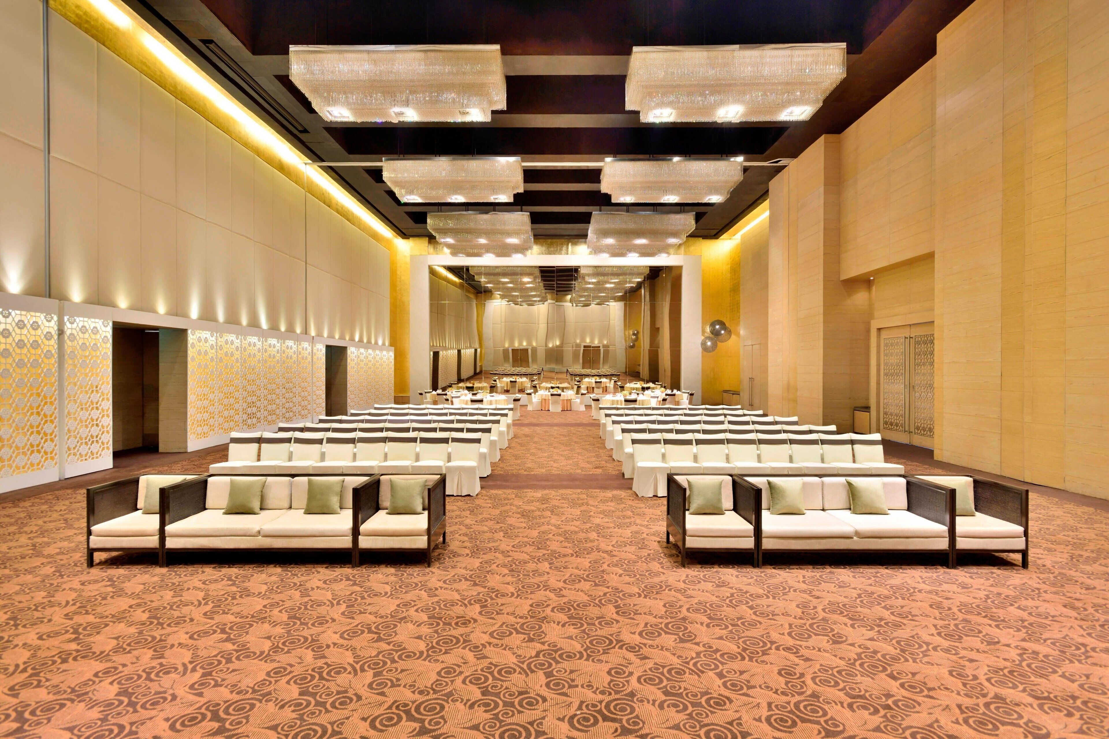 A conference room with rows of white sofas and tables, patterned carpet, and chandeliers.