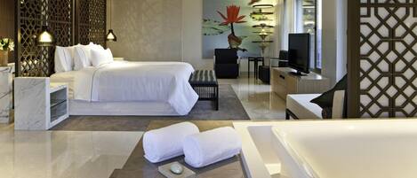 A modern hotel room with a large bed, a desk, a chair, a TV, and a bathtub.
