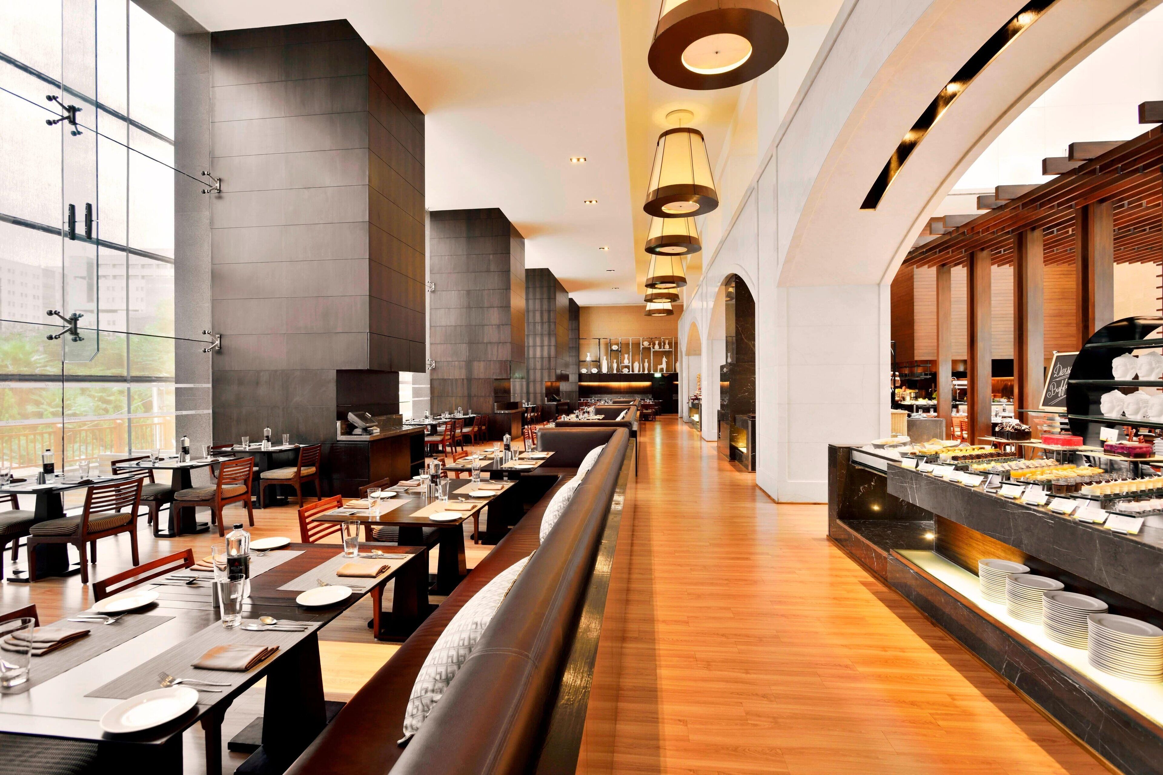 A spacious restaurant with high ceilings, modern lighting, and a long counter with a variety of food items.