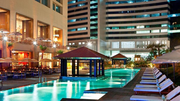 Un espace piscine d’hôtel avec des chaises longues, des parasols et un coin salon abrité.