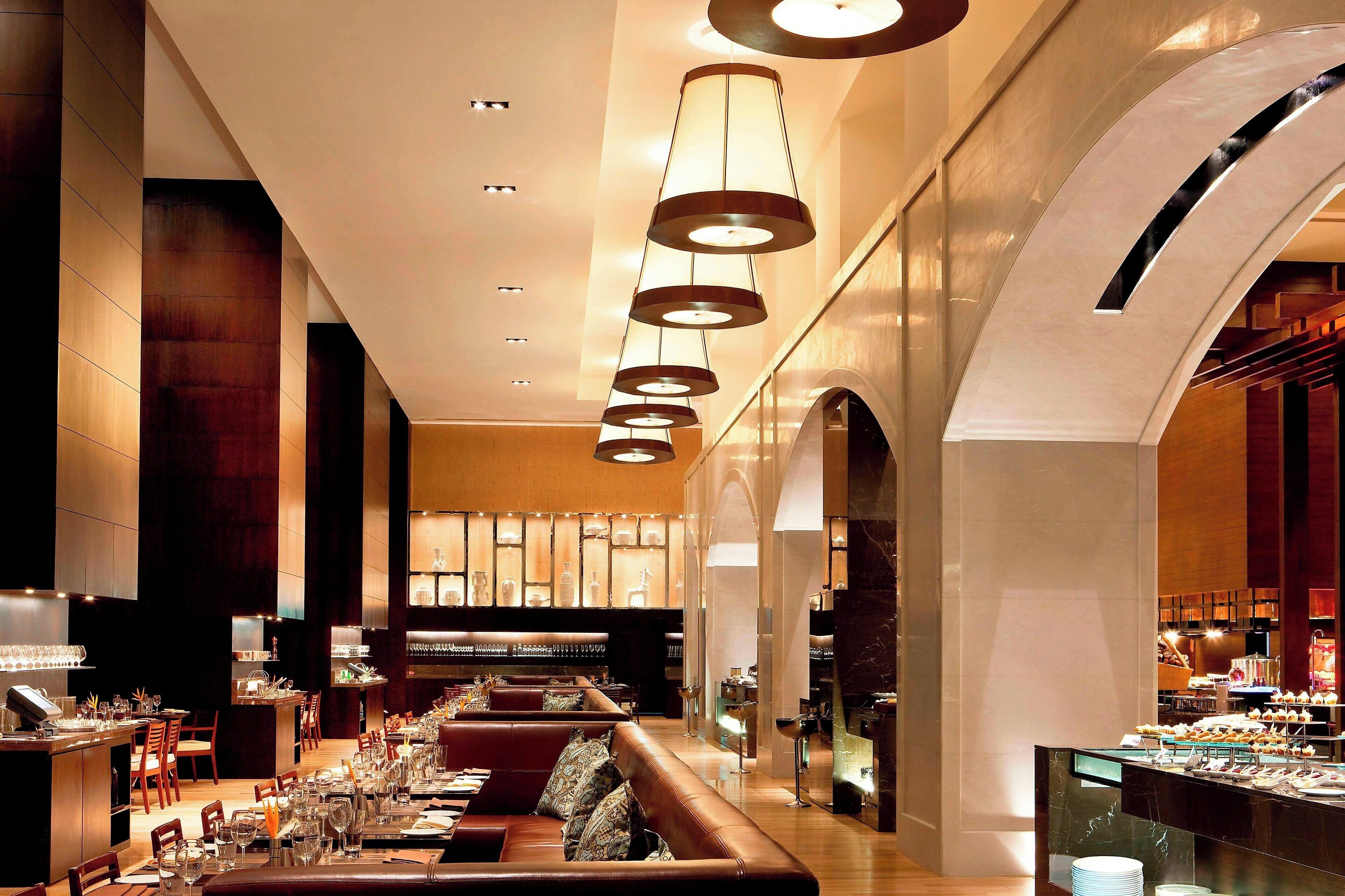 A spacious hotel lobby with a long reception desk, leather seating area, and a buffet counter.