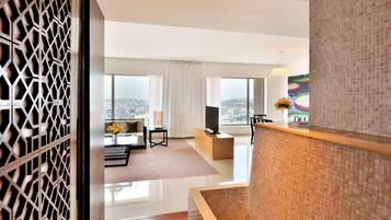 A modern hotel room with a city view, a flat-screen TV, a sofa, and a dining area with a view.