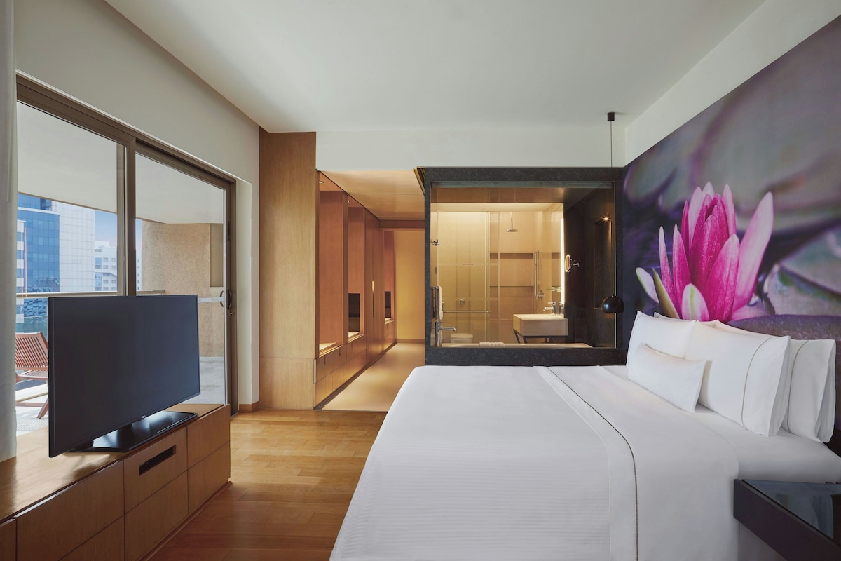 Een hotelkamer met een groot bed, een televisie, een bloemstilleven en uitzicht op de stad.