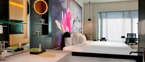 Una habitación de hotel moderna con una cama grande, un baño independiente con bañera, un espejo amplio y un televisor montado en la pared.