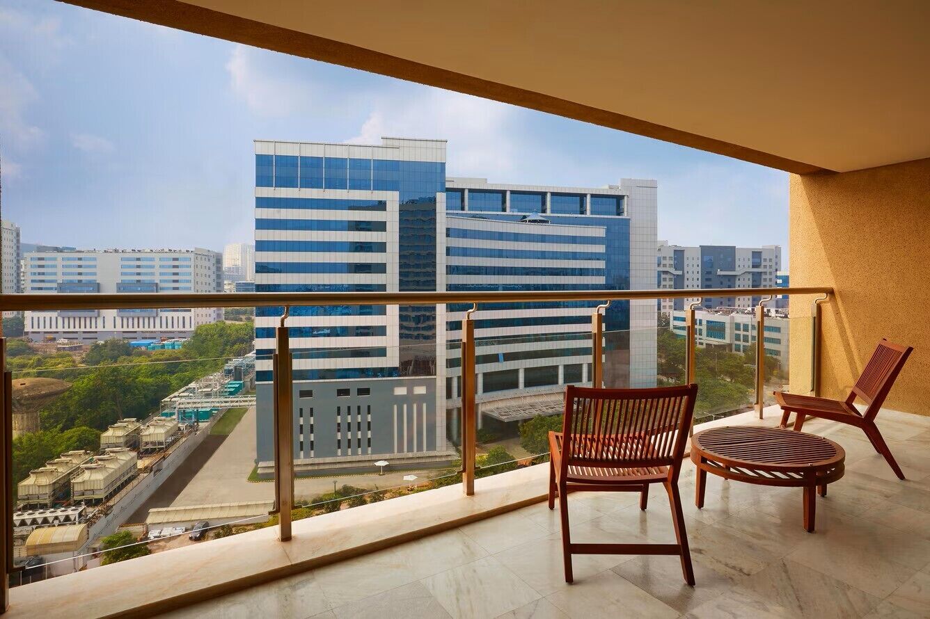 A balcony with a view of modern buildings, two wooden chairs, and a small round table.