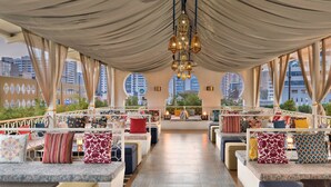 Un vaste espace intérieur aménagé avec de nombreuses tables et chaises, de grandes fenêtres offrant une vue sur la ville et un lustre décoratif suspendu au plafond.