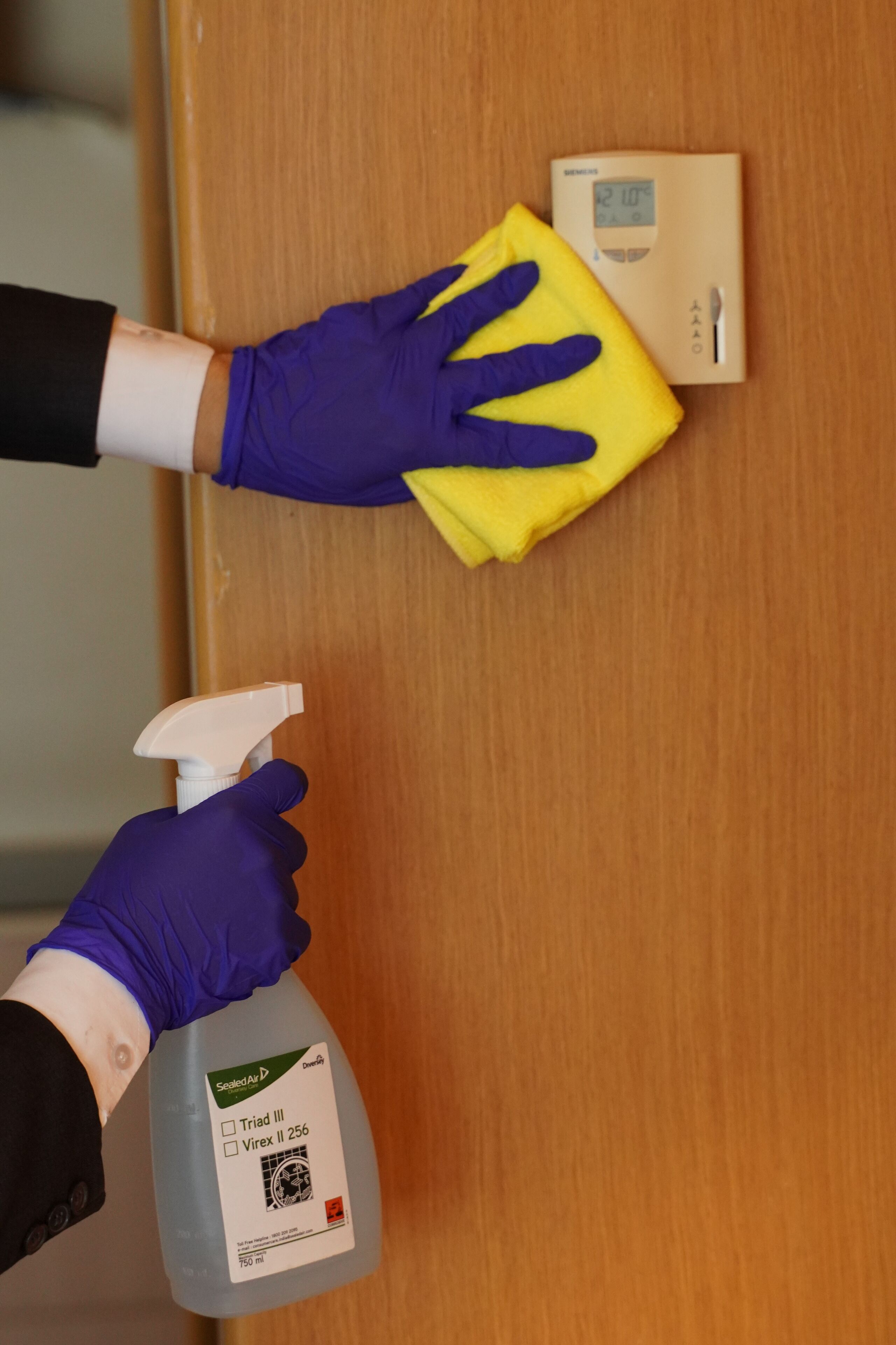 A person cleaning a wooden door with a yellow cloth and a spray bottle.