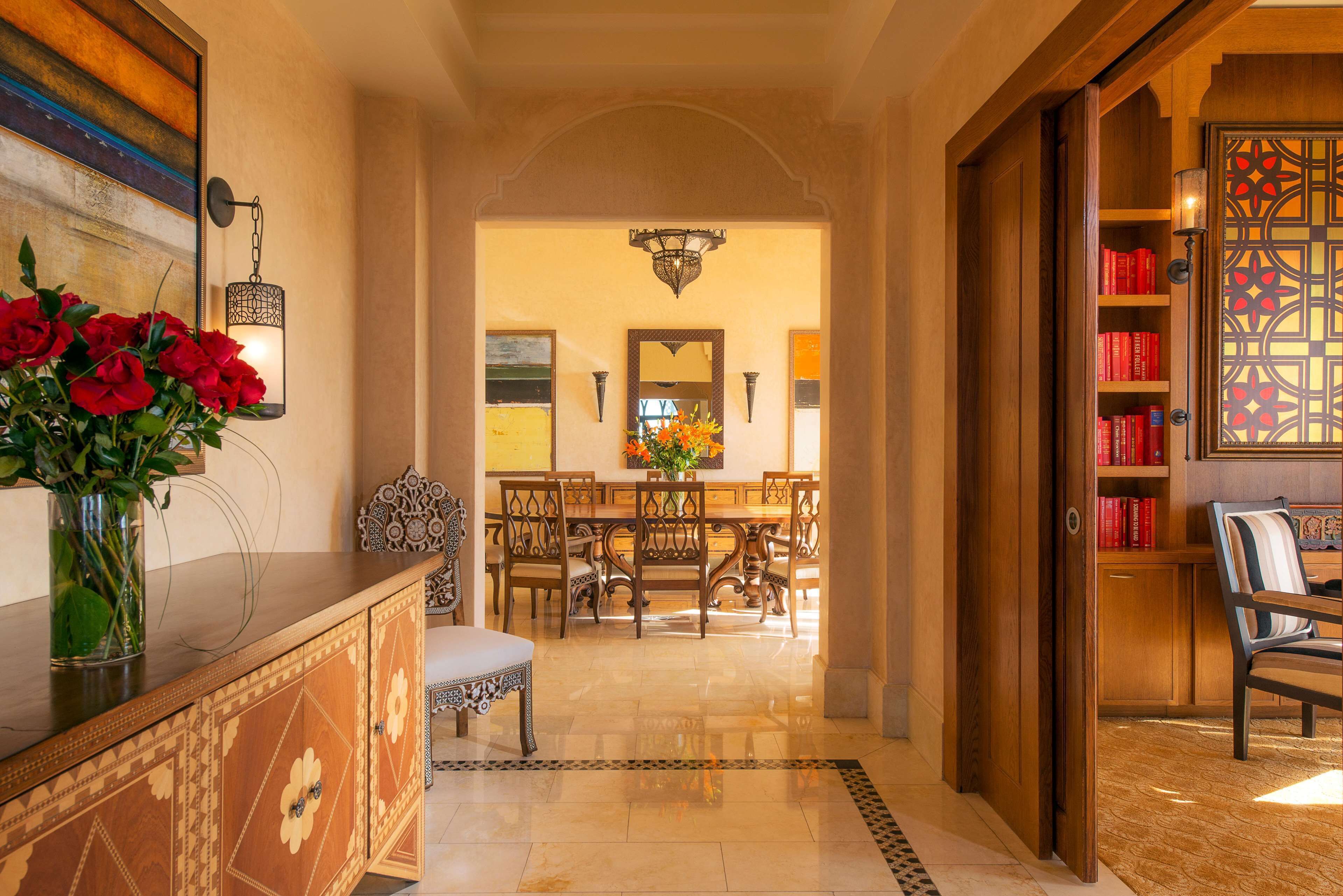 Un pasillo con una zona de comedor, una estantería y un espejo decorativo.